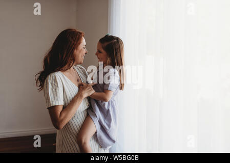 Side view of young mother holding young daughter and smiling at her Stock Photo