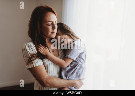Young mother cuddling with young daughter while closing eyes in studio Stock Photo