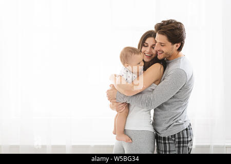 Loving parents cuddling with little baby son at window Stock Photo