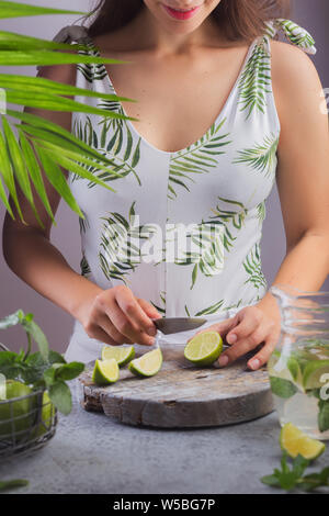 Girl prepares summer lemonade with lemon and mint, cuts lemon Stock Photo