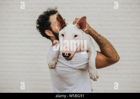 Bearded man holding a white bull terrier dog on shoulders Stock Photo