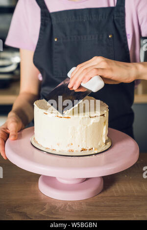 Young woman in dark apron and pink t-shirt smoothing cream on a top of Stock Photo