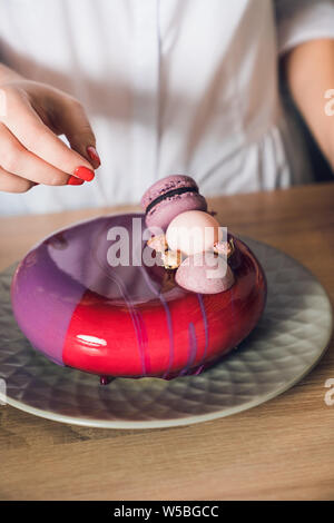Woman hands decorating pink cake by macaroons and flowers. Close up Stock Photo