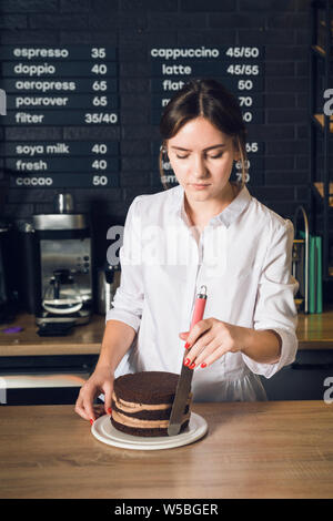 Young woman in white shirt  smoothing cream on a side of cake by spatu Stock Photo