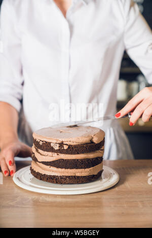 Woman's hands in white shirt  smoothing cream on a top of chocolate ca Stock Photo