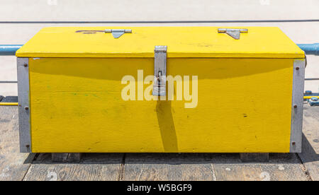 Yellow old wood box locked with rusty padlock. Bright yellow wood trunk on wooden deck, Santa Monica pier, California Stock Photo