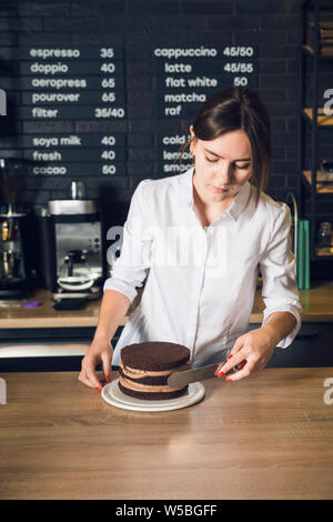 Young woman in white shirt  smoothing cream on a side of cake by spatu Stock Photo