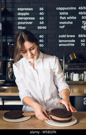 Young woman in white shirt bake a chocolate cake in cafeteria. Stock Photo