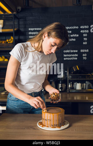 Beautiful woman in white t-shirt decorating chocolate cake with nuts Stock Photo