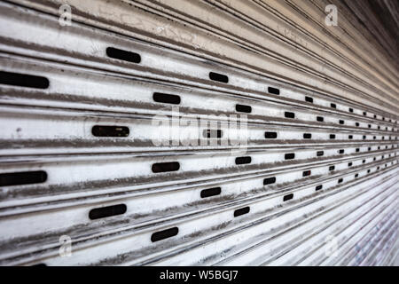 Old metal roller shutter white color faded full background texture. Garage or store entrance perspective view Stock Photo