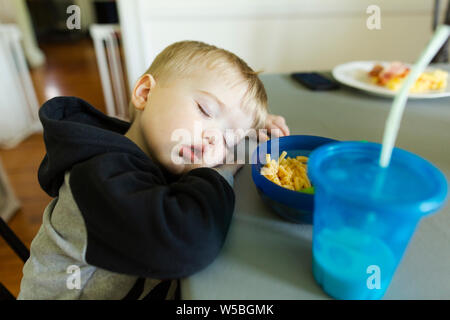 Close-up of blonde toddler boy sleeping with head on table at lunch Stock Photo