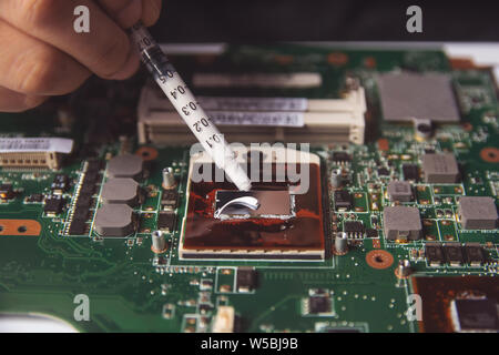 Technician applying thermal paste with syringe on the CPU processor on motherboard laptop Stock Photo