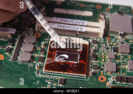 Technician applying thermal paste with syringe on the CPU processor on motherboard laptop Stock Photo