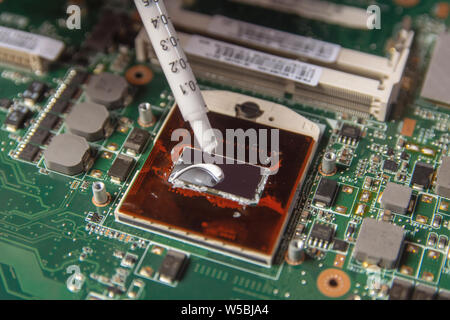 Technician applying thermal paste with syringe on the CPU processor on motherboard laptop Stock Photo