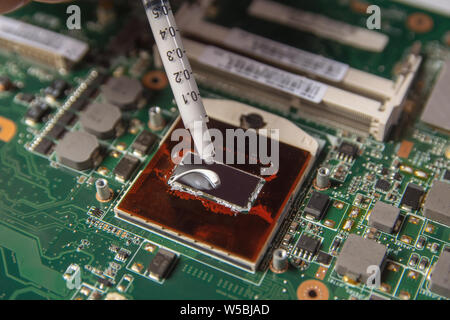 Technician applying thermal paste with syringe on the CPU processor on motherboard laptop Stock Photo