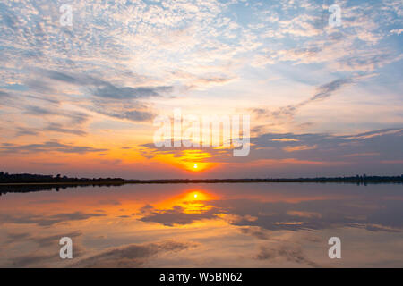 Sunset reflection lagoon. beautiful sunset behind the clouds and blue sky above the over lagoon landscape background. dramatic sky with cloud at sunse Stock Photo