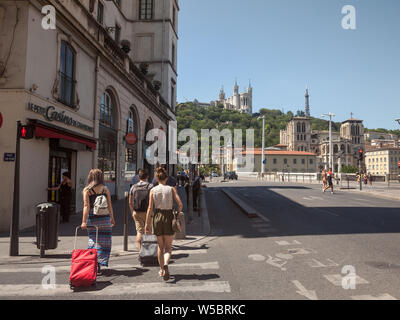LYON, FRANCE - JULY 19, 2019: Tourists walking with their luggage and suitcases in the city center of Lyon, with the iconic landmark of Notre Dame de Stock Photo