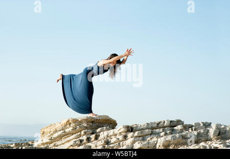 Woman in warrior 3 yoga pose by the sea. Stock Photo