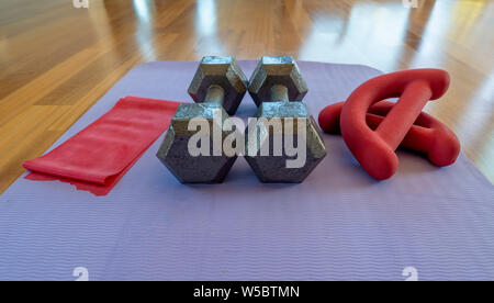 Close up of a pair of dumbbells, theraband exercise bands, and a yoga mat on hardwood floor Stock Photo