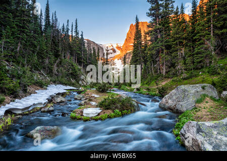 Fern creek flows out of Odessa Lake below Notchtop Mountain and the Ptarmigan Pass seen through the forest in Rocky Mountain National Park, Colorado. Stock Photo