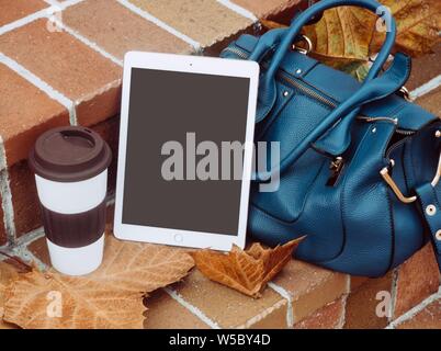 Shot of a white tablet besides a blue two-way leather bag and a cup placed on the stairs Stock Photo