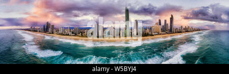 Pacific ocean waves rolling ashore of Surfers paradise suburb on Australian Gold Coast at sunrise with active board surfers riding the waves in front Stock Photo