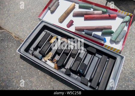 open boxes of black, greys, and color chalk on a blacktop walkway Stock Photo