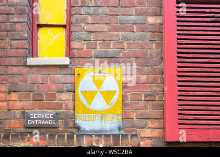 sign yellow white distressed fall shelter words and icon on an old urban city wall with red windows and shutters Stock Photo