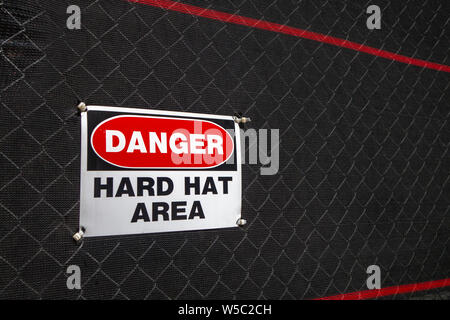 Danger hard hat area sign on a fenced in area covered with black mesh Stock Photo