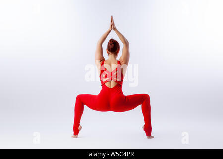 Beautiful slim woman in sports overalls  doing yoga, standing in an asana pose -legs apart, arms above head on white  isolated background. The concept Stock Photo