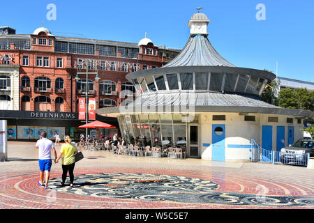 Couple holding hands walking in The Square & pebble mosaic pavement in Bournemouth town centre with Debenhams & Obscura street cafe Dorset England UK Stock Photo