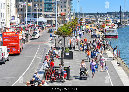 Poole Harbour view of summer season crowd of people seen from above walking along harbour promenade quay tour boat & marina beyond Dorset England UK Stock Photo