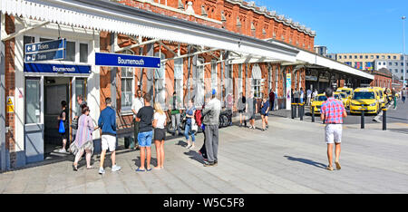 People outside ticket office & entrance to Bournemouth railway station brick building waiting to meet train passengers taxi rank beyond Dorset UK Stock Photo