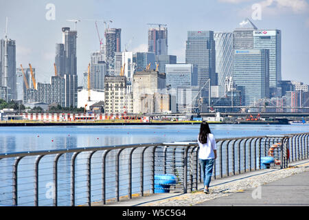 Teenage girl stands beside Royal Docks view looking across water to business development of Canary Wharf cityscape skyline in east London Docklands UK Stock Photo