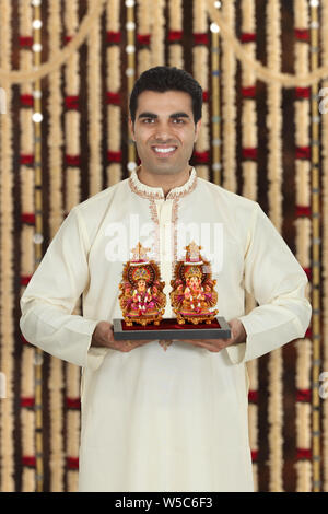 Man holding sculptures of Lakshmi and Ganesha and smiling Stock Photo