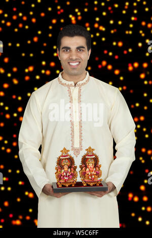 Man holding sculptures of Lakshmi and Ganesha and smiling Stock Photo