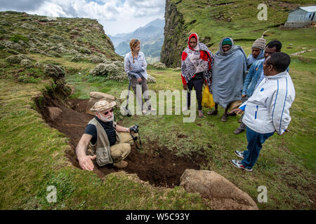 Local Ethiopian farmers look on as a field researcher examines the soil of a hillside, Debre Berhan, Ethiopia. Stock Photo