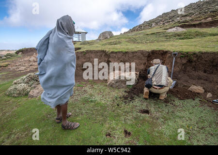 Local Ethiopian farmers look on as a field researcher examines the soil of a hillside, Debre Berhan, Ethiopia. Stock Photo