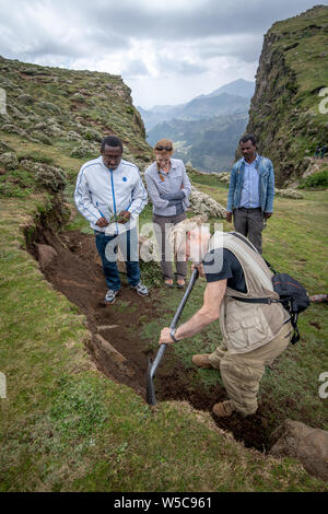 Local Ethiopian farmers look on as a field researcher examines the soil of a hillside, Debre Berhan, Ethiopia. Stock Photo