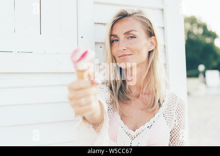 Young European woman holds melted strawberry ice cream in waffle cone in front of her. Stock Photo