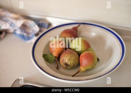 five pears in a plate with a blue border and a kitchen towel on the table. Stock Photo