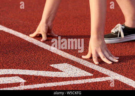 View of female athlete at race start. It stands on a red tartan track and is ready to run. Stock Photo