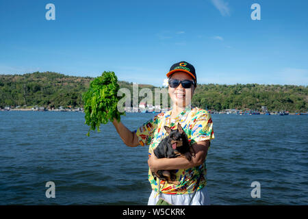 Phu Yen province, Vietnam - July 21, 2019: Female tourists smiling with a bunch of seaweed on hand in Phu Yen province, Vietnam. Seaweed is a favorite Stock Photo