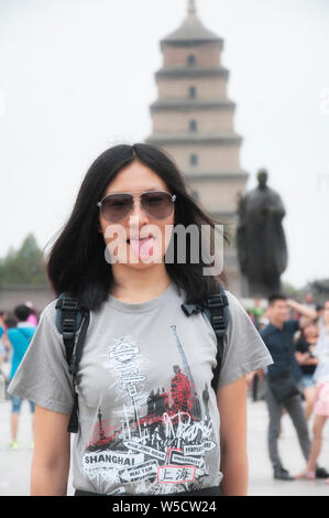 A playful chinese woman sticking her tongue out near Buddha statue near the Big wild goose pagoda in the city of Xian in Shaanxi province China. Stock Photo