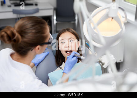High angle portrait of female dentist performing medical procedure on Asian girl, copy space Stock Photo