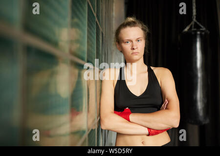 Waist up portrait of tough sportswoman looking at camera while leaning on glass wall in sports club, copy space Stock Photo