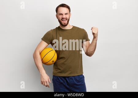 Young happy and excited man holding basket ball over isolated background . guy celebrating victory and raising hands, fan is rejoicing success of his Stock Photo