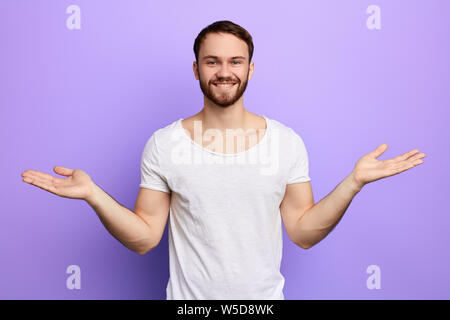 young cheerful happy handsome guy raising his hands with open palms, greeting gests, isolated blue background Stock Photo