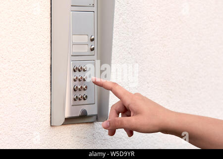 The hand of a young woman enters a numeric code on the keypad of an electronic lock or doorbell. Stock Photo