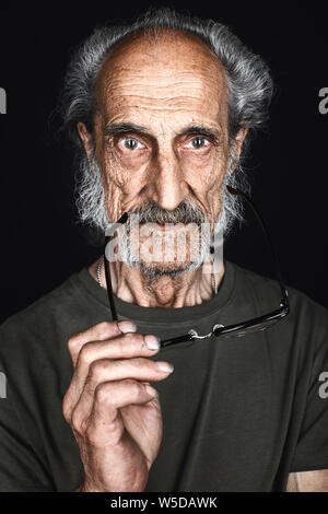 old experienced writer holding glasses and looking at the camera. close up photo. isolated black background. studio shot Stock Photo